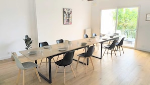A dining area with a long table, chairs, and a view of greenery outside.