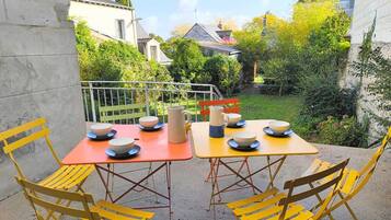 Ein Essbereich im Freien mit Tisch und Stühlen, umgeben von Grünflächen und Gebäuden.