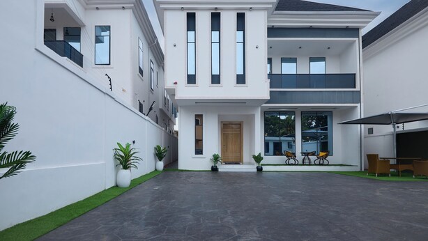 A modern two-story house with a flat roof, large windows, and a covered patio area with outdoor furniture. - Javes Luxury Residences (Lagos)