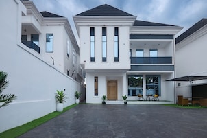 Uma casa moderna de dois andares com telhado plano, grandes janelas e um alpendre coberto com mobiliário de exterior.