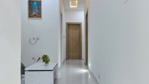 A modern hallway with a white reception desk, a framed cityscape picture, and a wooden door at the end. - Javes Luxury Residences (Lagos)