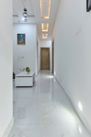 Um corredor moderno com uma receção branca, uma fotografia emoldurada de uma paisagem urbana e uma porta de madeira no final.
