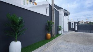 A modern building with a dark facade, a paved driveway, and potted plants along the side. - Javes Luxury Residences (Lagos)