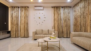 A living room with a beige sofa, a round coffee table with a remote control, and a decorative statue. - Javes Luxury Residences (Lagos)