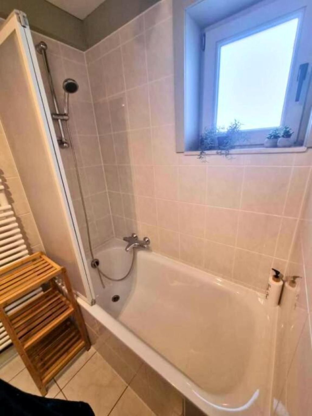 A bathroom with a bathtub, a shower, and a window with plants.