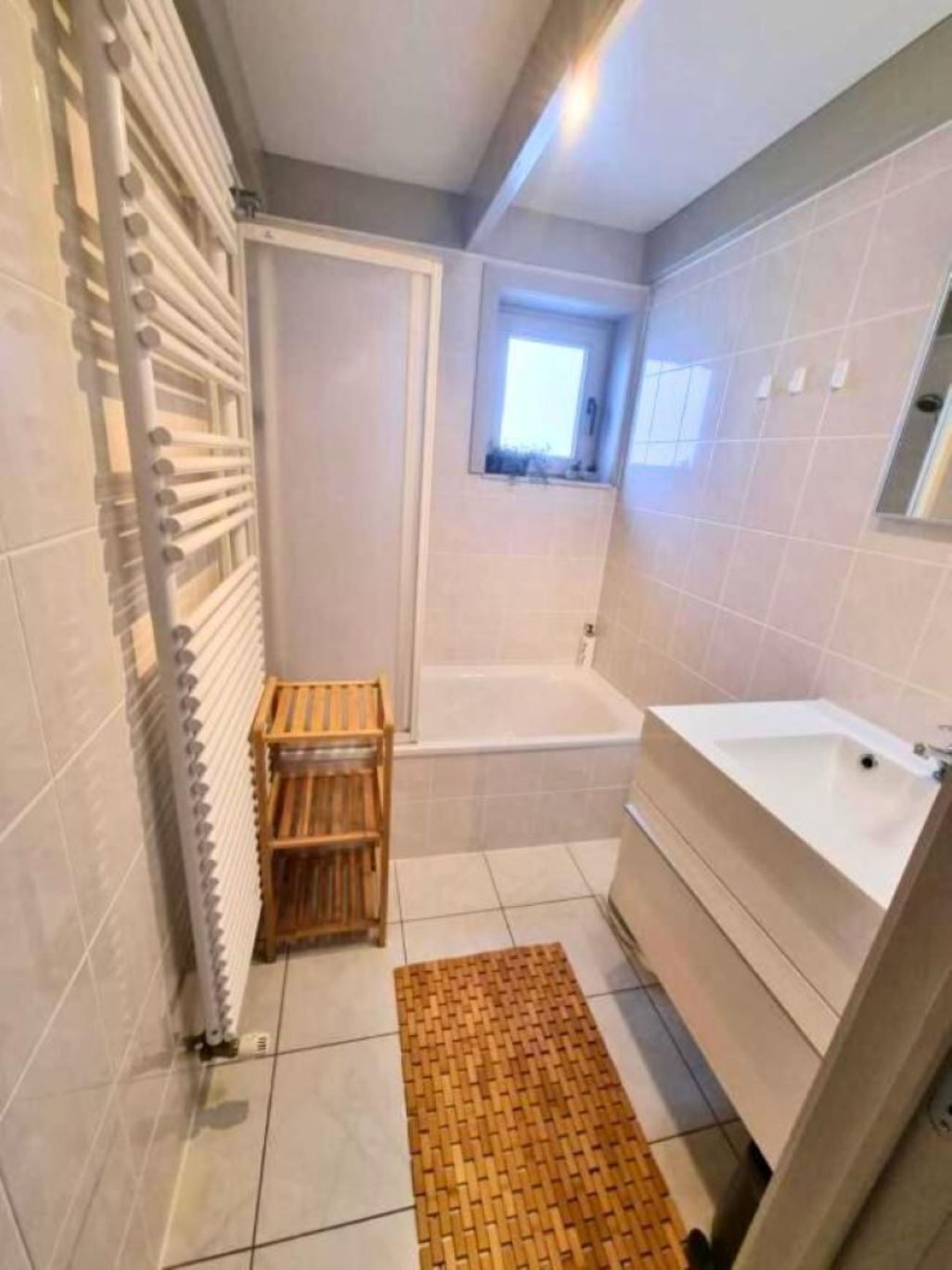 A modern bathroom with a bathtub, a wooden bench, and a small window.