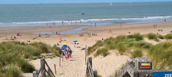 Ein Strand mit einer Holzpromenade, die zum Wasser führt, feinem Sand und einem klaren Himmel.