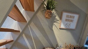 Una habitación acogedora con un escritorio de madera, una silla de mimbre, una planta colgante y un cartel enmarcado que dice "Beach House 68".