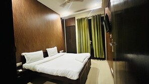 A hotel room with a wooden headboard, a bed with white bedding, a wardrobe, and green curtains. - Corporate Stayz (Gurugram)