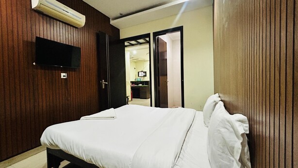 A hotel room with a bed, a TV mounted on the wall, and a door leading to a bathroom. - Corporate Stayz (Gurugram)