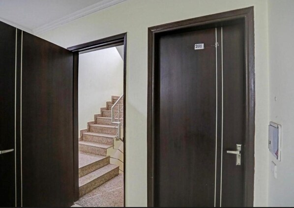 A hallway with two doors, one labeled 201, and a staircase leading to an upper floor. - Corporate Stayz (Gurugram)