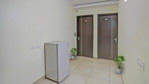 A hallway with two doors, a refrigerator, and potted plants. - Corporate Stayz (Gurugram)