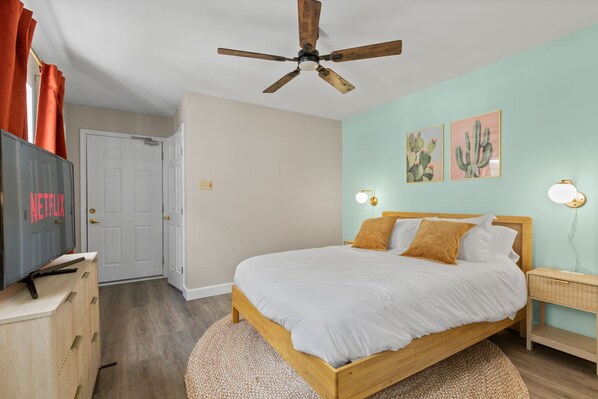 Un dormitorio con una cama de madera, un ventilador de techo, dos lámparas de pared y una puerta.