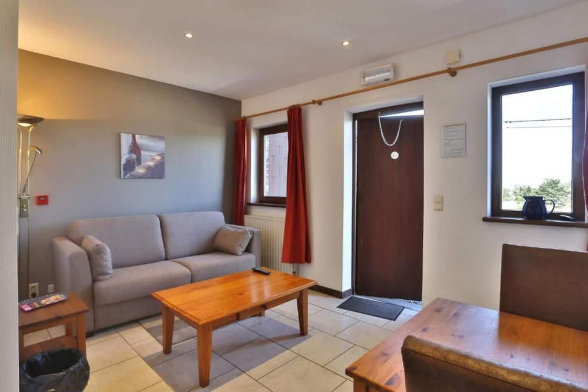 Una sala de estar con un sofá, una mesa de centro de madera y un ventanal con cortinas.