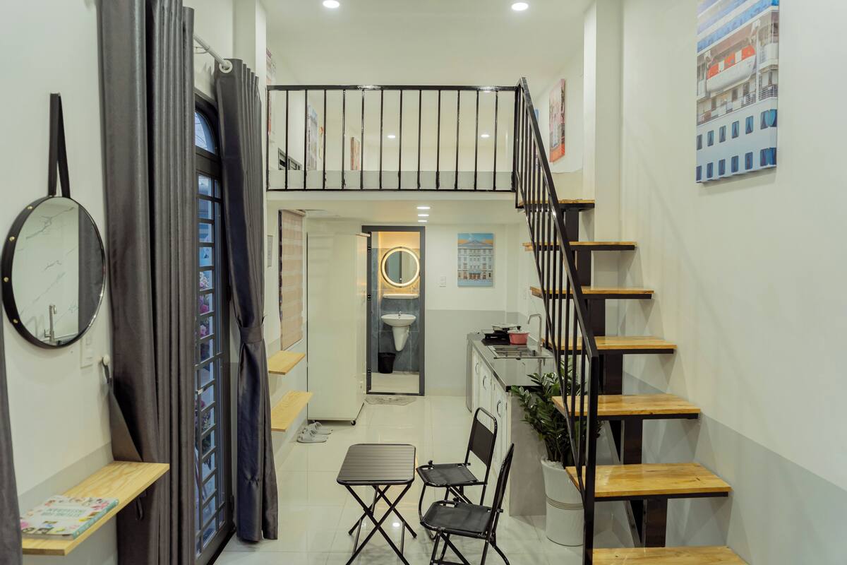 Une cuisine compacte avec un coin repas, un escalier et une petite salle de bain visible à travers une porte vitrée.