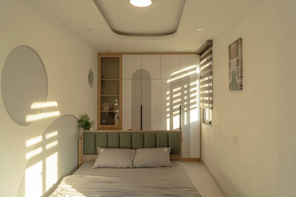 Une chambre à coucher comprenant un lit, une armoire intégrée, un miroir et une fenêtre avec des stores.