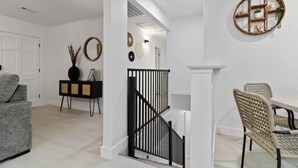 A modern living room with a grey sofa, a black console table, and a dining area with wicker chairs and a white table. - War Eagle Haven, Lake Access, spacious deck, games (Springdale)