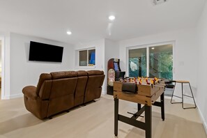 Un salon avec un canapé marron, une table de baby-foot et un téléviseur à écran plat fixé au mur.