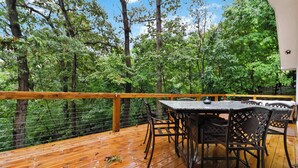 A wooden deck with a table and chairs, surrounded by a wooden railing and a view of a forest. - War Eagle Haven, Lake Access, spacious deck, games (Springdale)