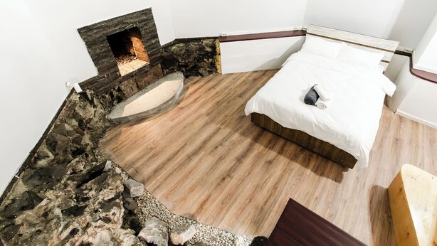 A bedroom with a stone fireplace, a bed with white bedding, and a wooden floor. - Hidden History - Modern Split-Level (Tbilisi)