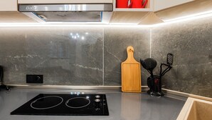 A kitchen with a black induction cooktop, a wooden cutting board, and a black spice rack. - Hidden History - Modern Split-Level (Tbilisi)
