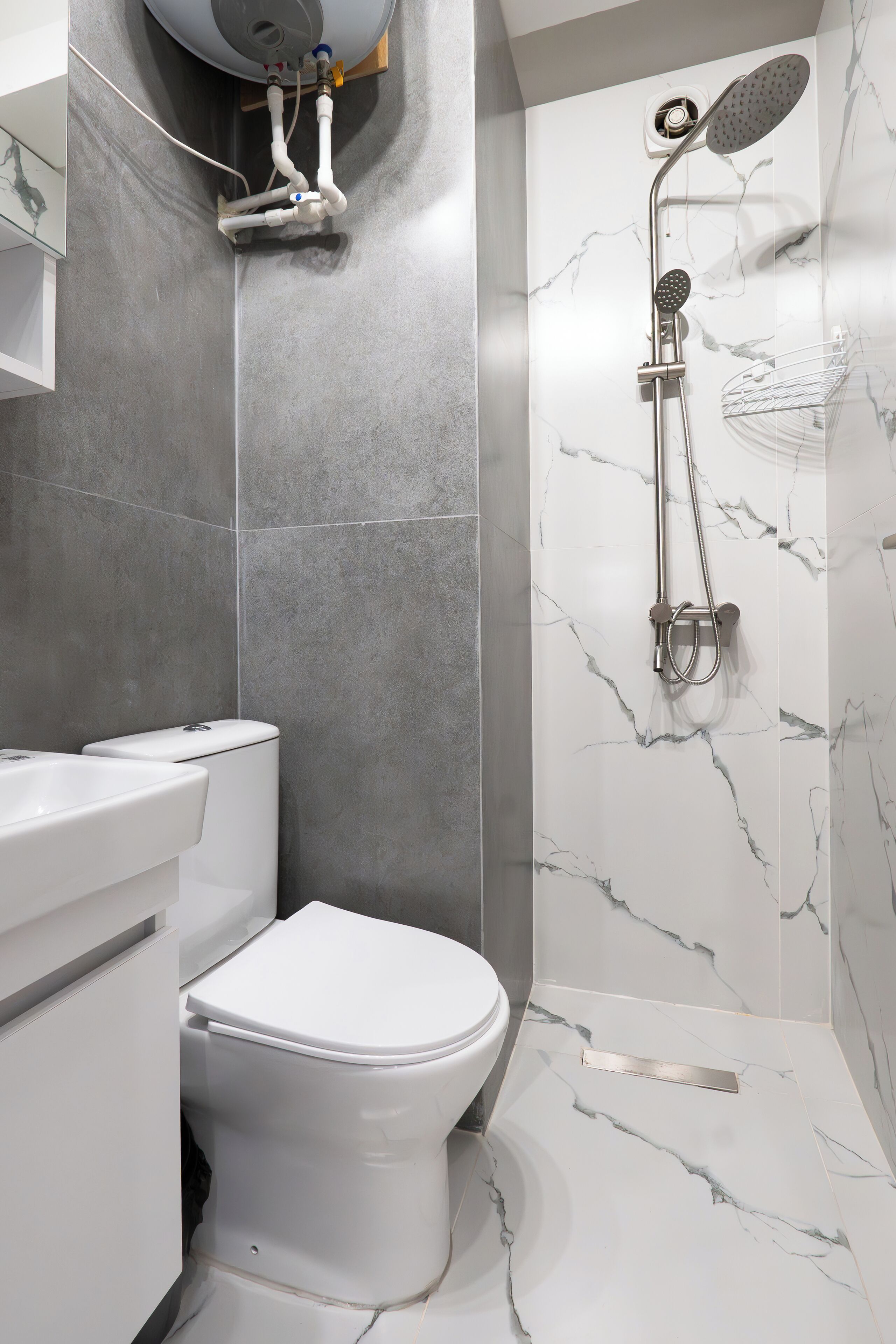 A modern bathroom with a toilet, a shower with a handheld showerhead, and a marble backsplash.