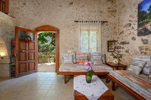 A cozy room with a stone wall, a wooden door, a sofa, a small table with a vase, and a window with curtains.
