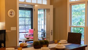 A dining area with a table set for four, a chair, and a view of the outdoors through a glass door. - Tree Covered Cottage - Walk to Douglas Beach! (Douglas)
