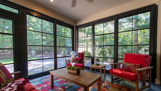 A sunroom with large windows, a wooden table, red chairs, and a colorful rug. - Tree Covered Cottage - Walk to Douglas Beach! (Douglas)