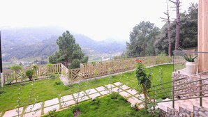 A garden with a stone pathway, a wooden fence, and a view of distant hills. - The Hoften Snowia Luxury Stay Near Bhalugarh Waterfall (Dhari)