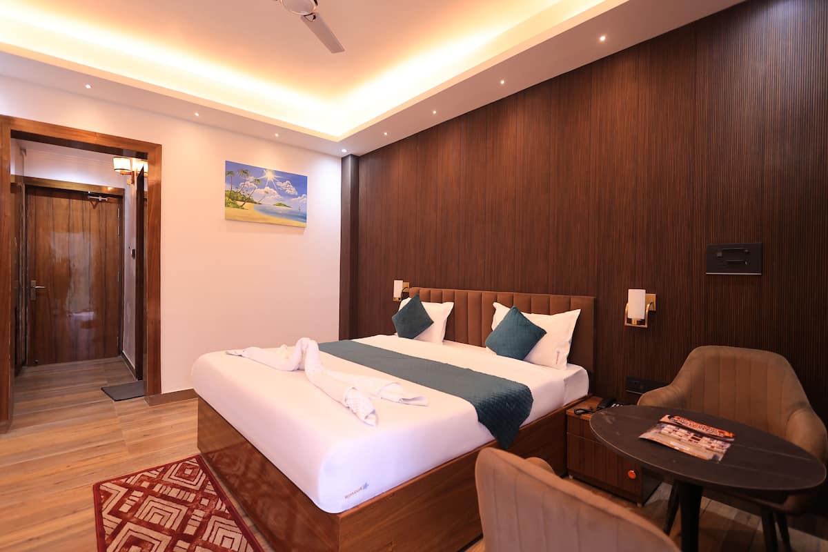 A hotel room with a large bed, a wooden headboard, a nightstand, a table, and a chair.
