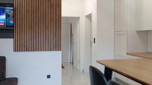 A modern kitchen with white cabinets, a wooden panel wall, and a television mounted on the wall. - Beautiful apartment in Seline with WiFi (Seline)