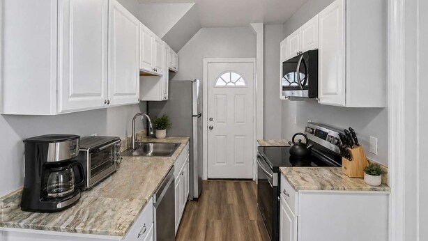 A compact kitchen with white cabinets, a built-in microwave, a coffee maker, and a kettle. - Division Champs 2 - All Star Baseball Rentals (Oneonta)
