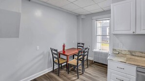 A room with a dining table, chairs, a radiator, and a window with blinds. - Division Champs 2 - All Star Baseball Rentals (Oneonta)