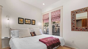 Une chambre avec un grand lit, une fenêtre avec des rideaux, un miroir fixé au mur et des œuvres d’art accrochées au mur.