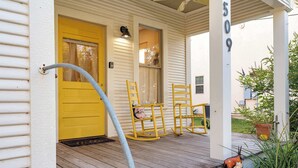 Un porche avec une porte jaune, deux fauteuils à bascule et le numéro « 509 » peint sur le mur.