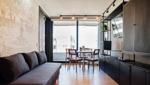 Eine moderne Küche mit Holzboden, einem dunkelgrauen Sofa und einem Essbereich mit Stühlen und einem Tisch.