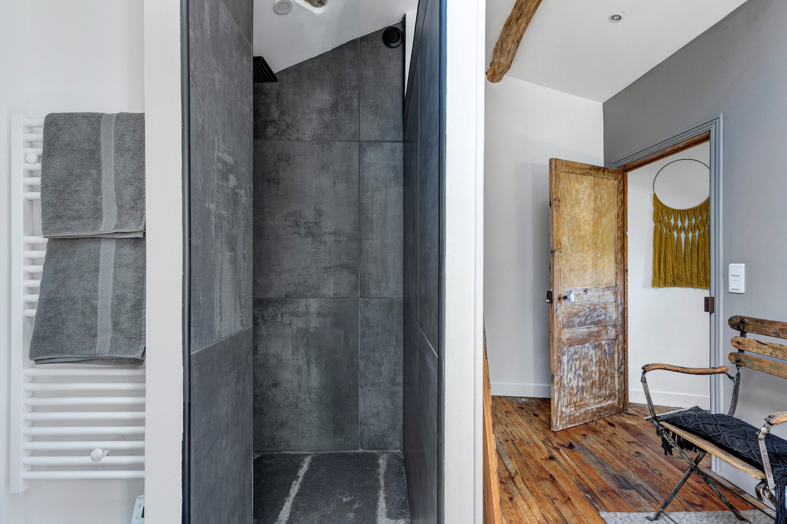 Un baño moderno con ducha, un banco y una puerta que da a otra habitación.