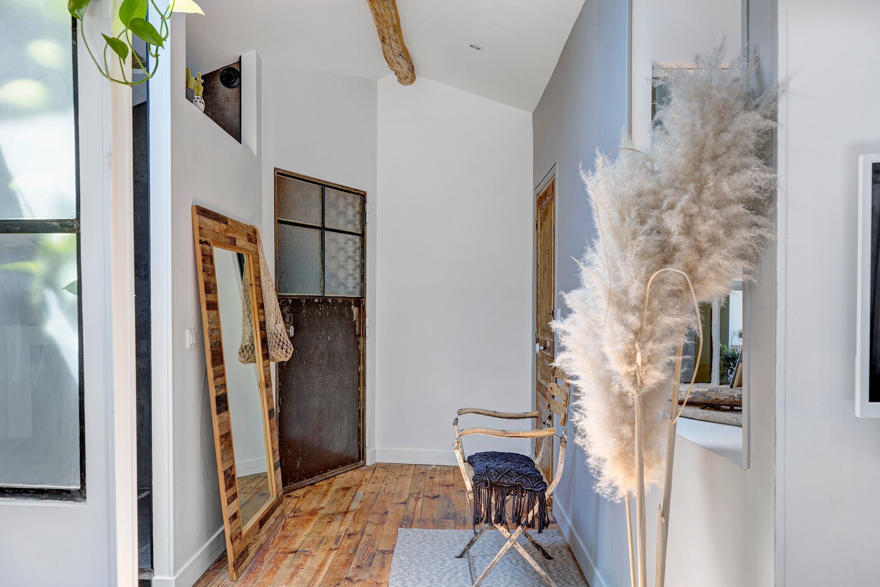 Un couloir avec un plancher en bois, une chaise, un miroir et une porte.