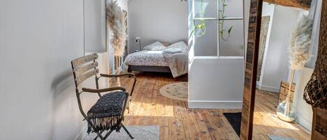 A room with a bed, a chair, a hanging plant, and a rustic wooden beam ceiling.
