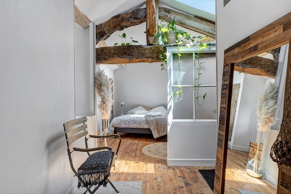 Ein Schlafzimmer mit Bett, Sessel, hängender Pflanze und rustikaler Holzbalkendecke.