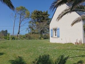 Ein weißes Gebäude mit blauen Fensterläden, umgeben von einer grünen Fläche mit weißen Blumen und Bäumen.
