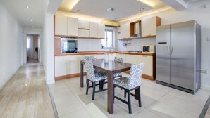 A modern kitchen with a dining area, featuring a central island, built-in appliances, and a stainless steel refrigerator.