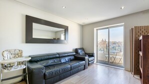 A modern living room with a black leather sofa, a small white side table, a high ceiling, and a large window with a city view.