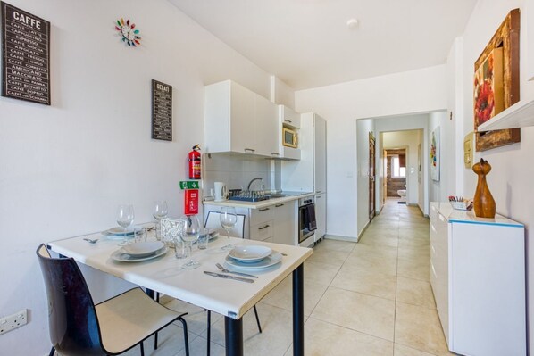 A modern kitchen with white cabinets, a built-in oven, and a dining area with a table set for four. - Seaview Comfort Apartment Gzira (Il-Gżira)