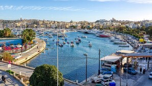 Uma marina com vários barcos atracados, céu claro e paisagem urbana ao fundo.
