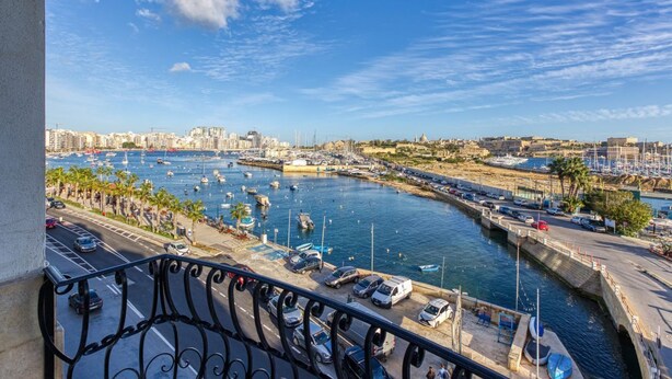Uma marina com barcos atracados, céu claro e paisagem urbana ao fundo.