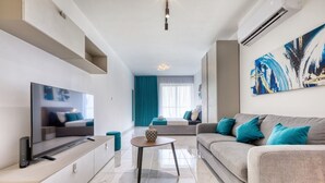 A modern living room with a flat-screen TV, a grey sofa with teal cushions, a small coffee table, and a large abstract painting on the wall.