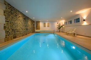 Una piscina interna con pareti in pietra, una terrazza solarium e una poltrona prendisole.