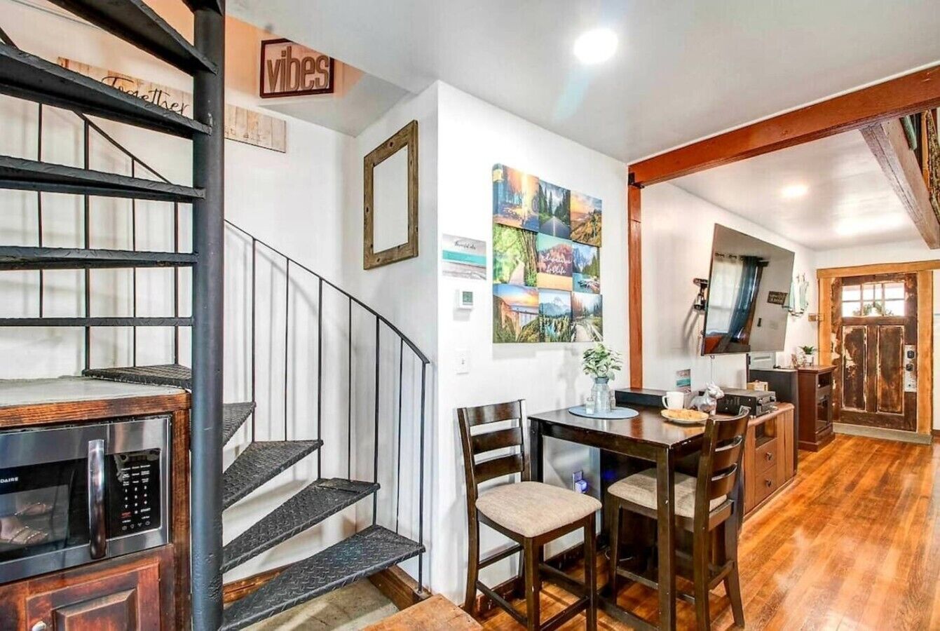 A kitchen with a wooden table, chairs, a microwave, and a staircase with a railing.